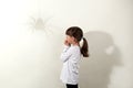 Childhood fears. Side view of small dark haired girl wearing white casual shirt having fear of insects, looking at shadow of