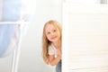 Childhood, fun and people concept - happy smiling beautiful little girl hiding behind room door. The child plays hide and seek at