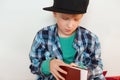 Childhood and leisure. Image of schoolboy in stylish checked shirt and cap opening red book isolated over white background wanting Royalty Free Stock Photo