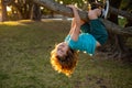 Childhood leisure and kids activities concept. Child hanging upside down on tree and having fun in summer park. Happy