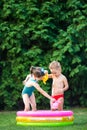 Childhood summer games with water pool. Caucasian brother and sister play with plastic toys watering can pouring water splashing, Royalty Free Stock Photo