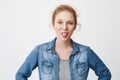 Childish emotive redhead teenage girl sticking out tongue and smiling, make faces while standing with hands on waist Royalty Free Stock Photo