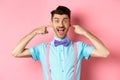 Childish funny guy shut ears and laughing at camera, refuse to listen, standing ignorant on pink background