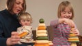Teacher plays pyramids with children on table. She holds the baby in her arms.