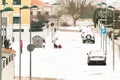 Children and adults play in the snow on a snowy and foggy street.