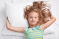 Children, awakening and bed time concept. Little adorable relaxed girl, dressed in casual outfit, feels relaxed in comfortable bed