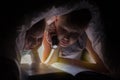 Children bedtime. Sister and brother are reading a book under a blanket with flashlight. Royalty Free Stock Photo