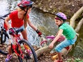 Children with bicycle help each other cross river on log. Royalty Free Stock Photo