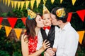 Children birthday party. Family father and mother hold son of one year of birth in arms and kiss cheekin the background of park an