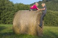 Children blond girl and boy (siblings) resting on hay bale, summer, holiday, relaxing, playing Royalty Free Stock Photo
