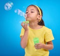 Children, blue background and a girl blowing bubbles in studio for fun or child development of motor skills. Kids, game