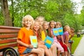 Children with blue notebooks sit in row on bench