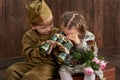 Children boy are dressed as soldier in retro military uniforms and girl in pink dress sitting on old suitcase, dark wood backgroun Royalty Free Stock Photo