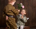 Children boy are dressed as soldier in retro military uniforms and girl in pink dress sitting on old suitcase, dark wood backgroun Royalty Free Stock Photo