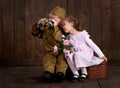 Children boy are dressed as soldier in retro military uniforms and girl in pink dress sitting on old suitcase, dark wood backgroun Royalty Free Stock Photo