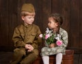 Children boy are dressed as soldier in retro military uniforms and girl in pink dress sitting on old suitcase, dark wood backgroun Royalty Free Stock Photo