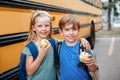 Children boy and girl students friends eating apples healthy snack by yellow school bus outdoor. Education and back to school in Royalty Free Stock Photo