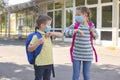 Children, a boy and a girl, wearing masks, greet their elbows on the street in the schoolyard due to the coronavirus epidemic. Royalty Free Stock Photo