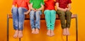 Children in bright and colorful clothes sit barefoot with their legs dangling to the bottom