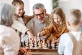 Children brother and sister playing chess while sitting in living room with senior grandparents