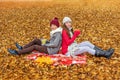 Children brother and sister are sitting with their backs to each other on a plaid in an autumn park and holding cups with hot tea