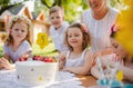 Children with cake standing around table on birthday party in garden in summer. Royalty Free Stock Photo