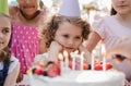 Children with cake standing around table on birthday party in garden in summer. Royalty Free Stock Photo