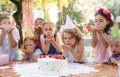 Children with cake standing around table on birthday party in garden in summer. Royalty Free Stock Photo
