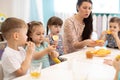 Children and carer together eat fruit as a snack in the kindergarten, daycare or school