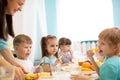 Children and carer together eat fruits and vegetables in kindergarten or daycare