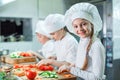 Children in chef`s hat grind vegetables on the kitchen.