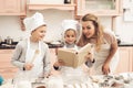 Children with mother in kitchen. Family is reading recipe in cookbook.