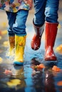 Children with colorful gum boots splashing water in muddy puddles.