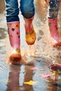 Children with colorful gum boots splashing water in muddy puddles.