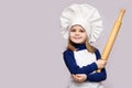 Children cook. Happy little girl in chef uniform holds rolling pin on white background. Royalty Free Stock Photo