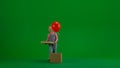 Little girl in jeans overall and ponytail on chroma key green screen isolated background, opens box red balloon popping