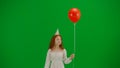 Little girl in white dress with red balloon on chroma key green screen isolated background in party hat walking looking Royalty Free Stock Photo