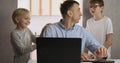 Children distract dad from work. Young male freelancer trying to work at home with two children.