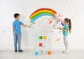 Children drawing rainbow on white wall