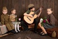 Children are dressed in retro military uniforms sitting and playing guitar, sending a soldier to the army, dark wood background, r Royalty Free Stock Photo