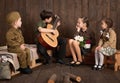 Children are dressed in retro military uniforms sitting and playing guitar, sending a soldier to the army, dark wood background, r Royalty Free Stock Photo