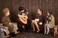 Children are dressed in retro military uniforms sitting and playing guitar, sending a soldier to the army, dark wood background, r Royalty Free Stock Photo