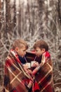 Children drink hot chocolate under warm blanket in winter forest. Christmas vacation.