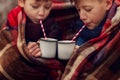 Children drink hot chocolate under warm blanket in winter forest. Christmas vacation.