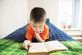 Children education, boy reading book lying on bed, child portrait smiling with book, interesting storybook Royalty Free Stock Photo