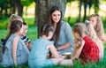 Children and education, young woman at work as educator reading book to boys and girls in park. Royalty Free Stock Photo