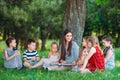 Children and education, young woman at work as educator reading book to boys and girls in park. Royalty Free Stock Photo