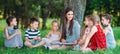 Children and education, young woman at work as educator reading book to boys and girls in park. Royalty Free Stock Photo