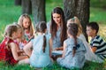 Children and education, young woman at work as educator reading book to boys and girls in park. Royalty Free Stock Photo