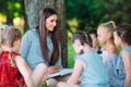 Children and education, young woman at work as educator reading book to boys and girls in park. Royalty Free Stock Photo